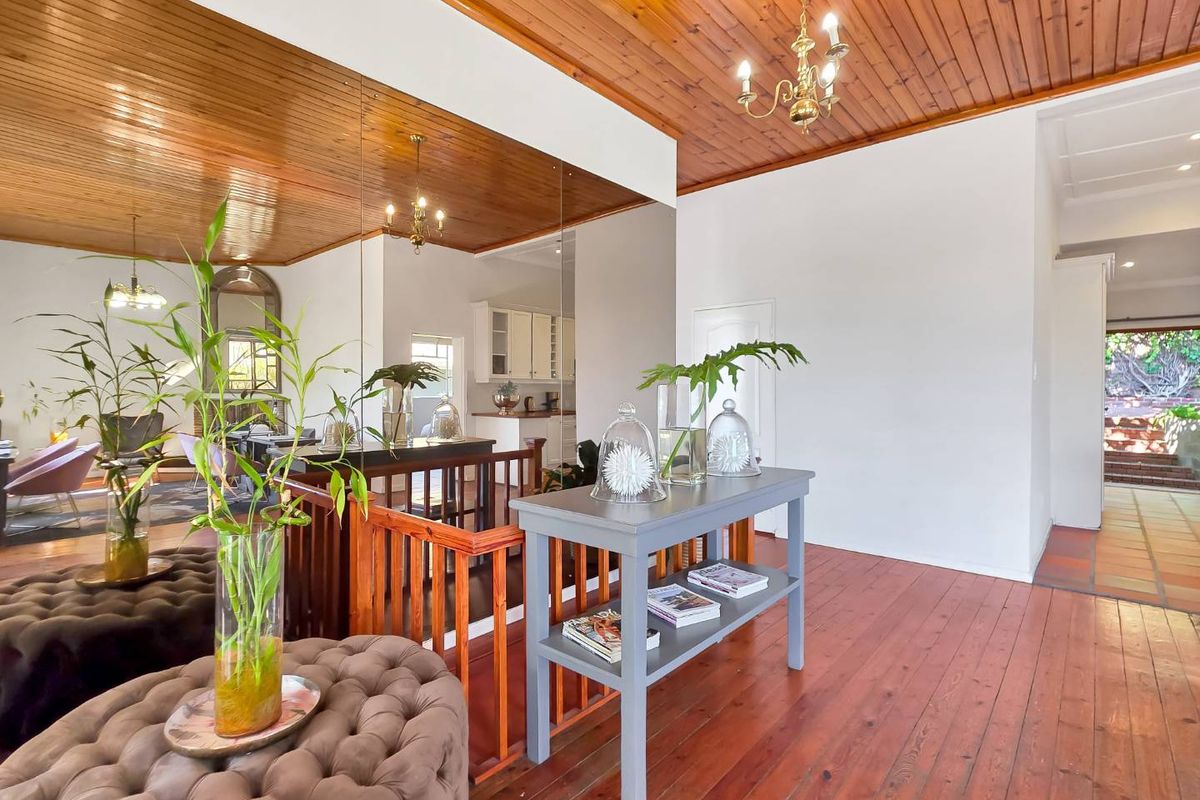 Spacious living area featuring warm timber ceilings and flooring, a classic timber balustrade, and a large feature mirror reflecting the adjacent kitchen space.