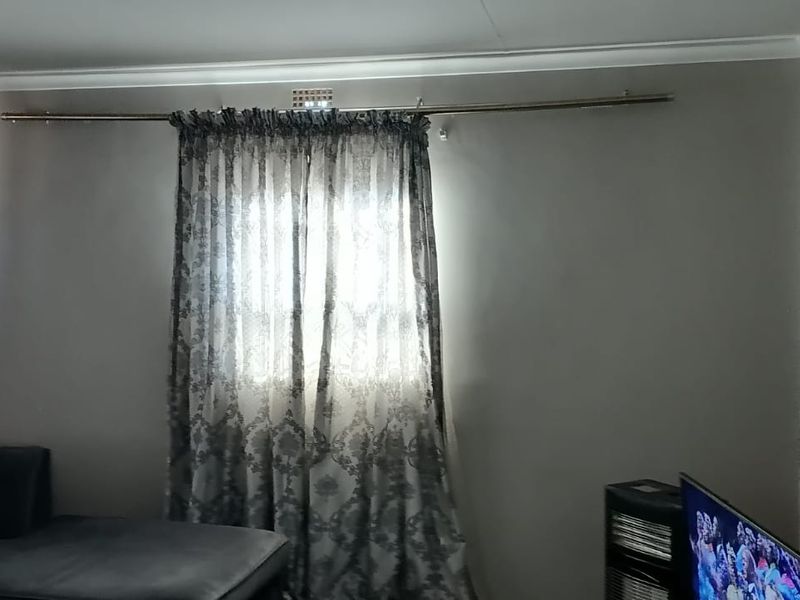 A living room area featuring neutral wall paint, decorative cornice detailing, and a window fitted with a curtain rod.