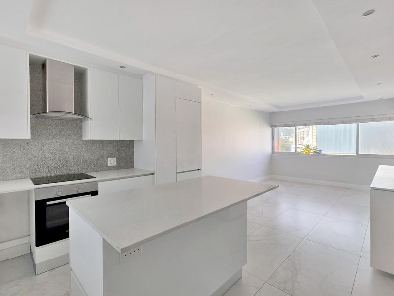 Modern open-plan kitchen and living area featuring sleek white cabinetry, stone countertops, integrated appliances, and bright tiled flooring throughout.