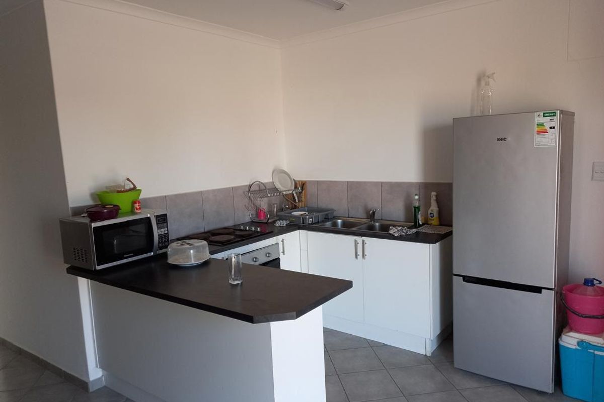 A functional kitchen featuring white cabinetry, dark countertops, a built-in hob, and tiled flooring, offering a practical layout for daily meal preparation.