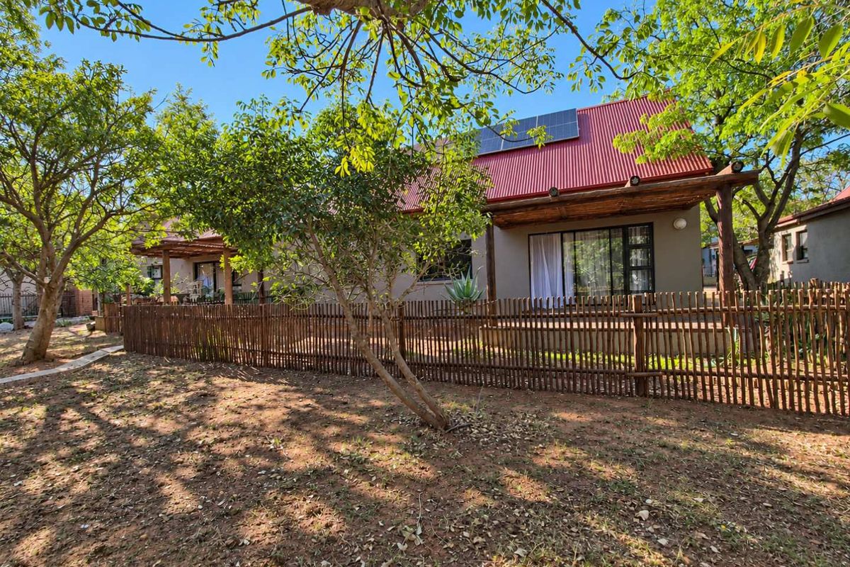 Rear view of the townhouse featuring a corrugated metal roof with solar panels, a timber pergola, and a private fenced garden area.