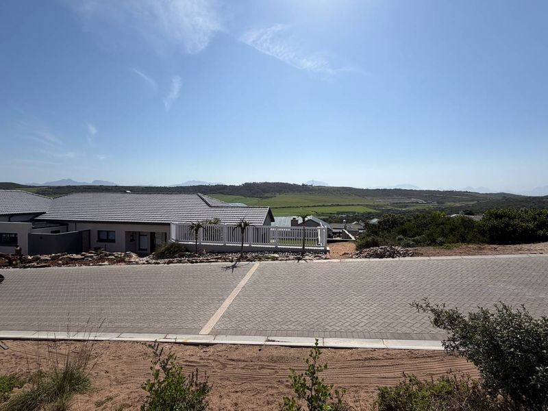 A scenic view overlooking a residential street with paved driveway, neat landscaping, and distant mountain vistas under a clear blue sky.