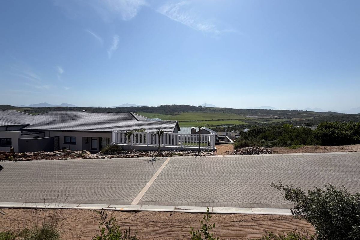 A scenic view overlooking a residential street with paved driveway, neat landscaping, and distant mountain vistas under a clear blue sky.