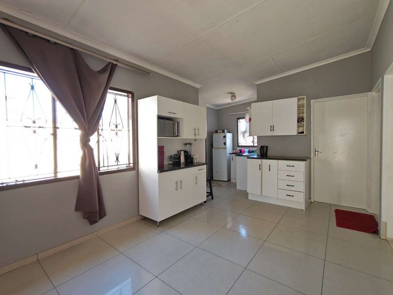 A functional kitchen featuring white built-in cabinetry, laminate countertops, and tiled flooring, with natural light provided by a window with security bars.