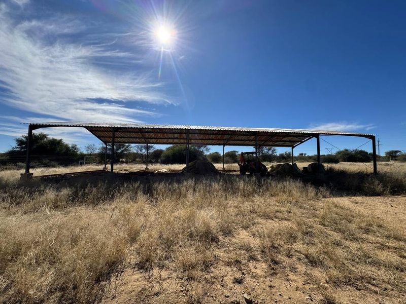 An open-sided agricultural utility structure with a corrugated metal roof and steel frame, situated on a rural small holding.