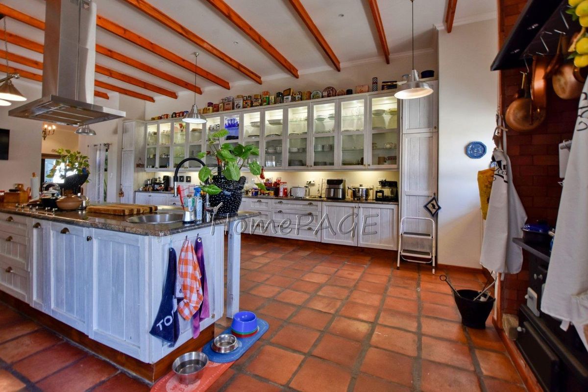 Spacious farmhouse-style kitchen featuring a large central island, extensive built-in cabinetry with glass-fronted display units, and exposed timber ceiling beams.
