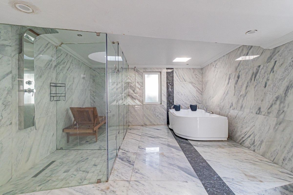 Spacious luxury bathroom featuring floor-to-ceiling marble tiling, a large glass-enclosed walk-in shower, and a built-in corner jetted bathtub.