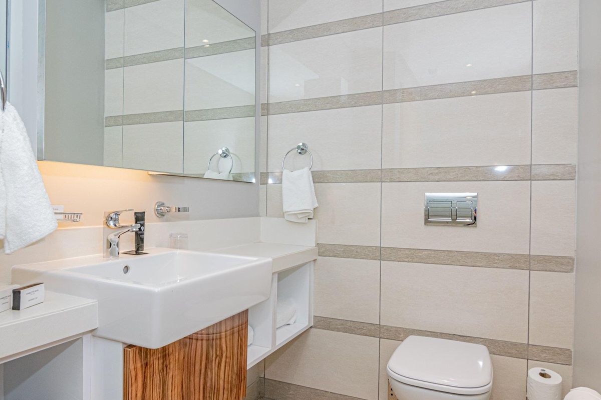 Modern bathroom featuring a wall-mounted toilet, sleek vanity with integrated basin, and large wall-mounted mirror with integrated lighting.