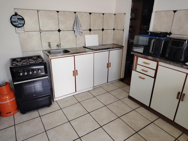 A functional kitchen area featuring a gas stove, stainless steel sink, tiled backsplash, and built-in cabinetry with tiled flooring.