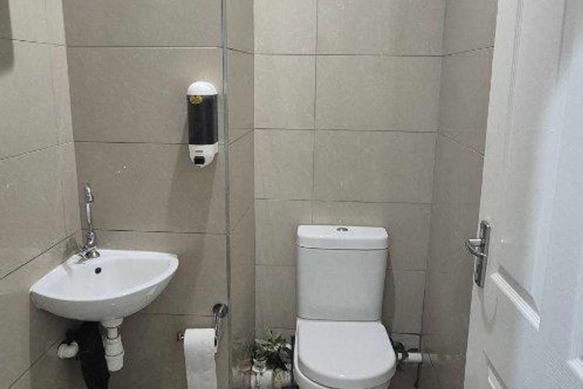 A compact office restroom featuring floor-to-ceiling wall tiles, a wall-mounted corner basin, and a standard toilet suite.