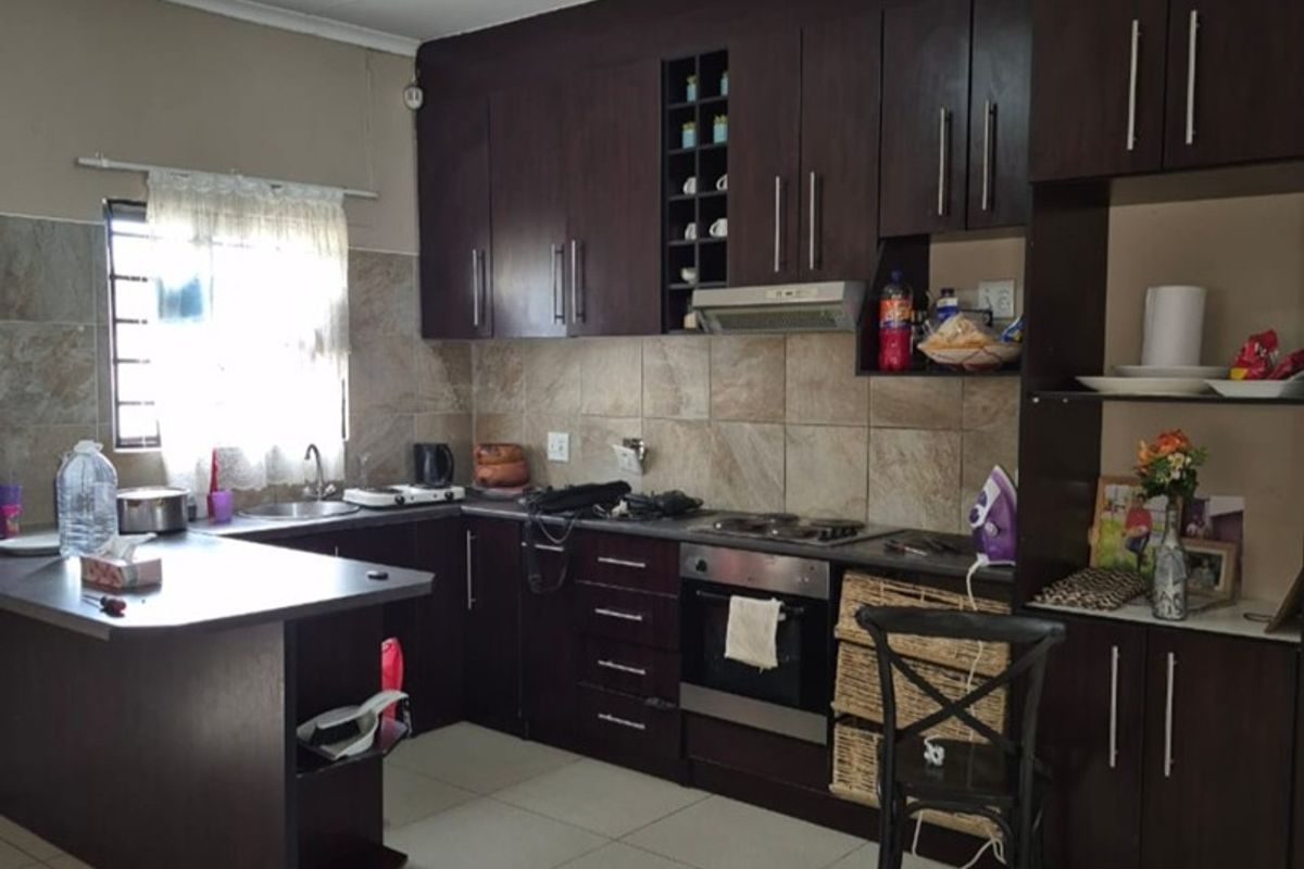 A functional kitchen featuring dark wood cabinetry, a built-in oven with hob, tiled backsplash, and a convenient kitchen island with tiled flooring throughout.