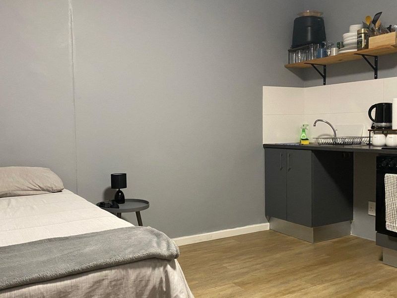 Compact open-plan studio apartment featuring a kitchenette with built-in oven, sink, and tiled splashback, finished with modern laminate flooring.