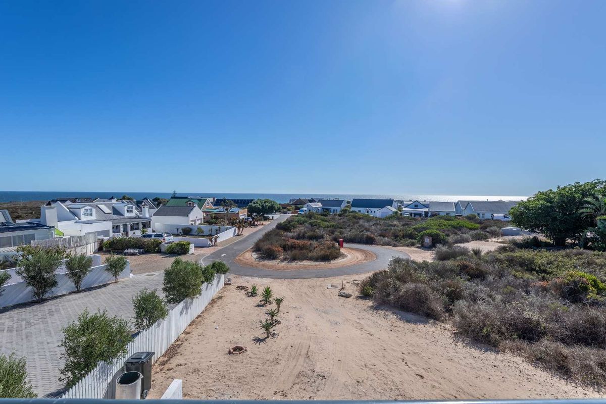 Elevated aerial view of the coastal residential estate, showcasing the surrounding neighborhood, paved roads, and proximity to the ocean.