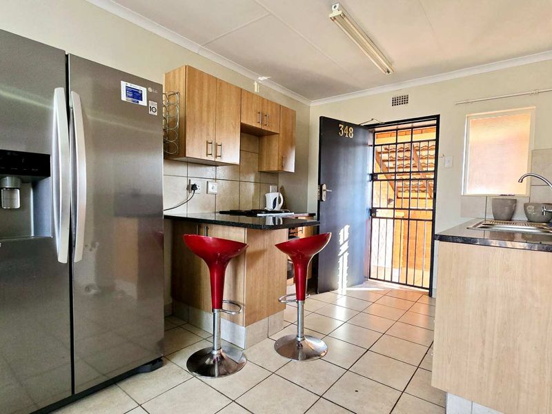 Compact kitchen featuring light wood cabinetry, granite countertops, tiled flooring, and a security gate at the entrance.