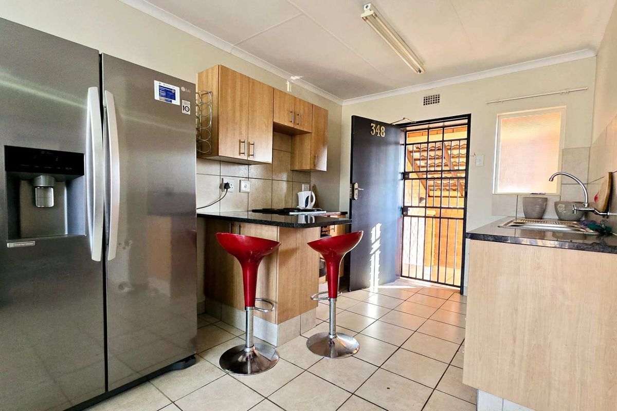 Compact kitchen featuring light wood cabinetry, granite countertops, tiled flooring, and a security gate at the entrance.