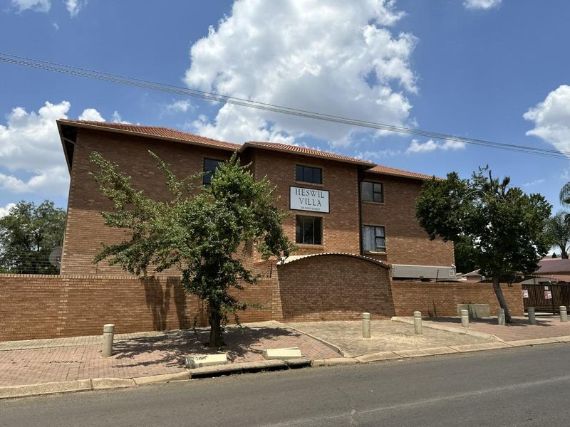 Front exterior view of Heswil Villa apartment complex featuring a face brick facade, tiled roof, and secure perimeter walling.