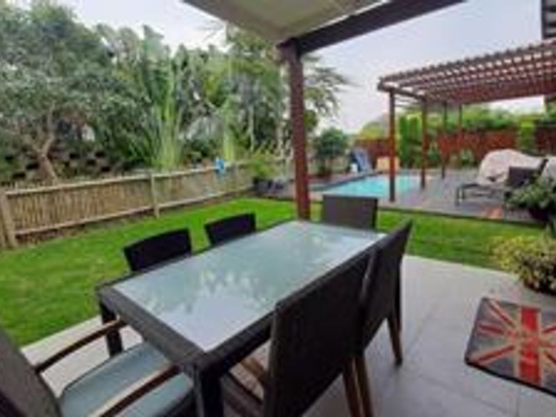 A covered patio area featuring tiled flooring and a timber pergola, overlooking a private swimming pool and landscaped garden.
