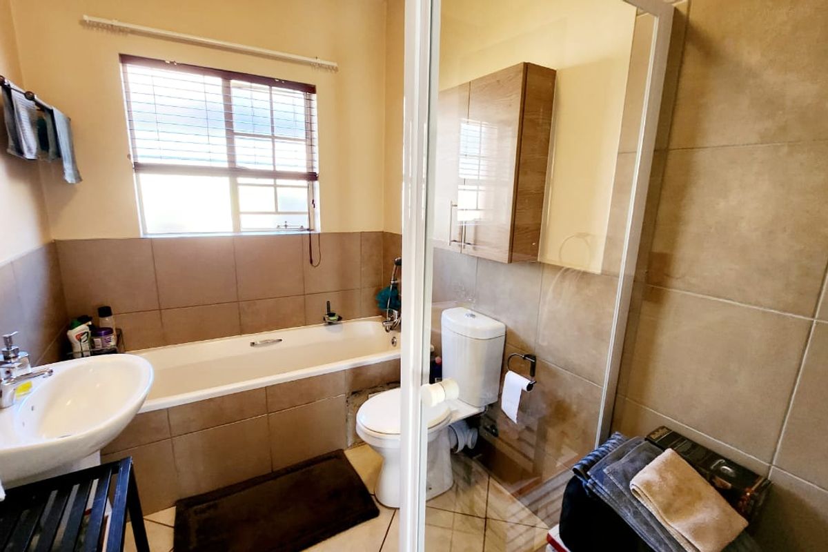 A functional bathroom featuring a bathtub, separate shower enclosure, pedestal basin, and wall-mounted storage cabinetry with neutral wall and floor tiling.
