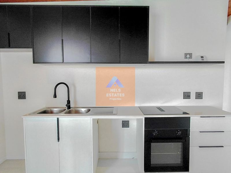 Modern kitchen featuring sleek black upper cabinetry, white lower cabinets, integrated oven and hob, and a contemporary black sink fixture.