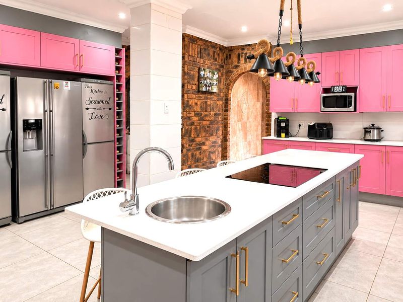 Modern kitchen featuring a central island with induction cooktop, stone countertops, vibrant pink cabinetry, and a distinctive exposed brick feature wall.