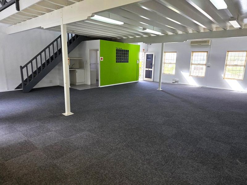 Spacious open-plan office area featuring a mezzanine level, staircase, kitchenette, and carpeted flooring, providing a versatile workspace environment.
