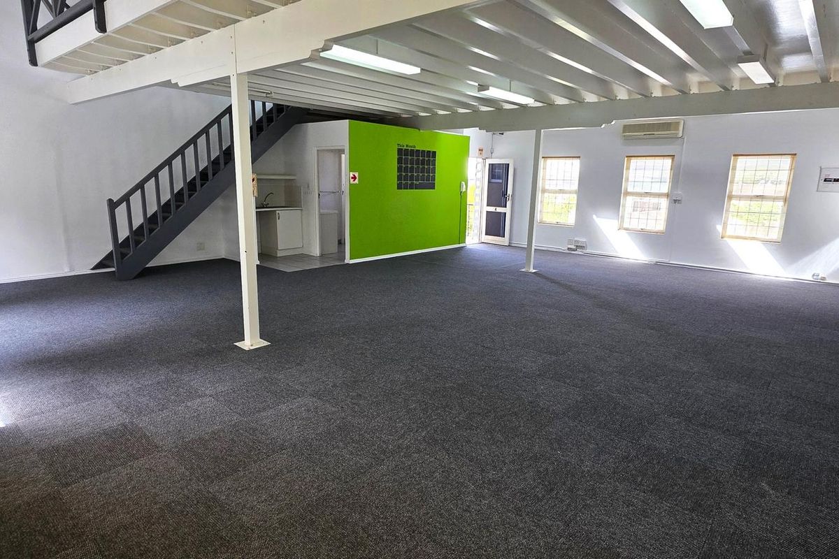 Spacious open-plan office area featuring a mezzanine level, staircase, kitchenette, and carpeted flooring, providing a versatile workspace environment.