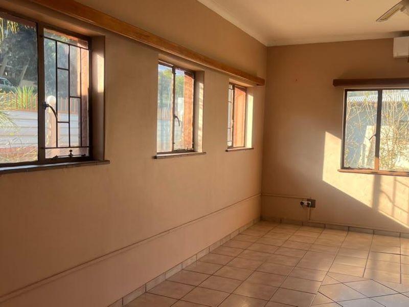 An empty living room featuring tiled flooring, a ceiling fan, wall-mounted air conditioning, and large windows with security bars.