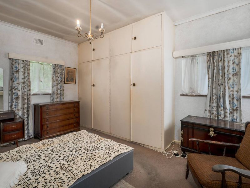 A bedroom featuring built-in floor-to-ceiling cupboards, carpeted flooring, and dual windows with traditional window treatments.