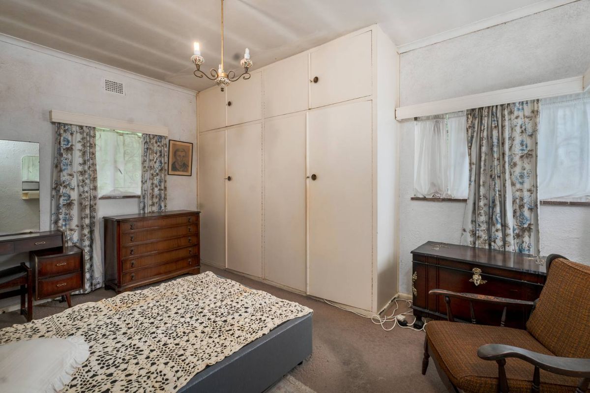 A bedroom featuring built-in floor-to-ceiling cupboards, carpeted flooring, and dual windows with traditional window treatments.