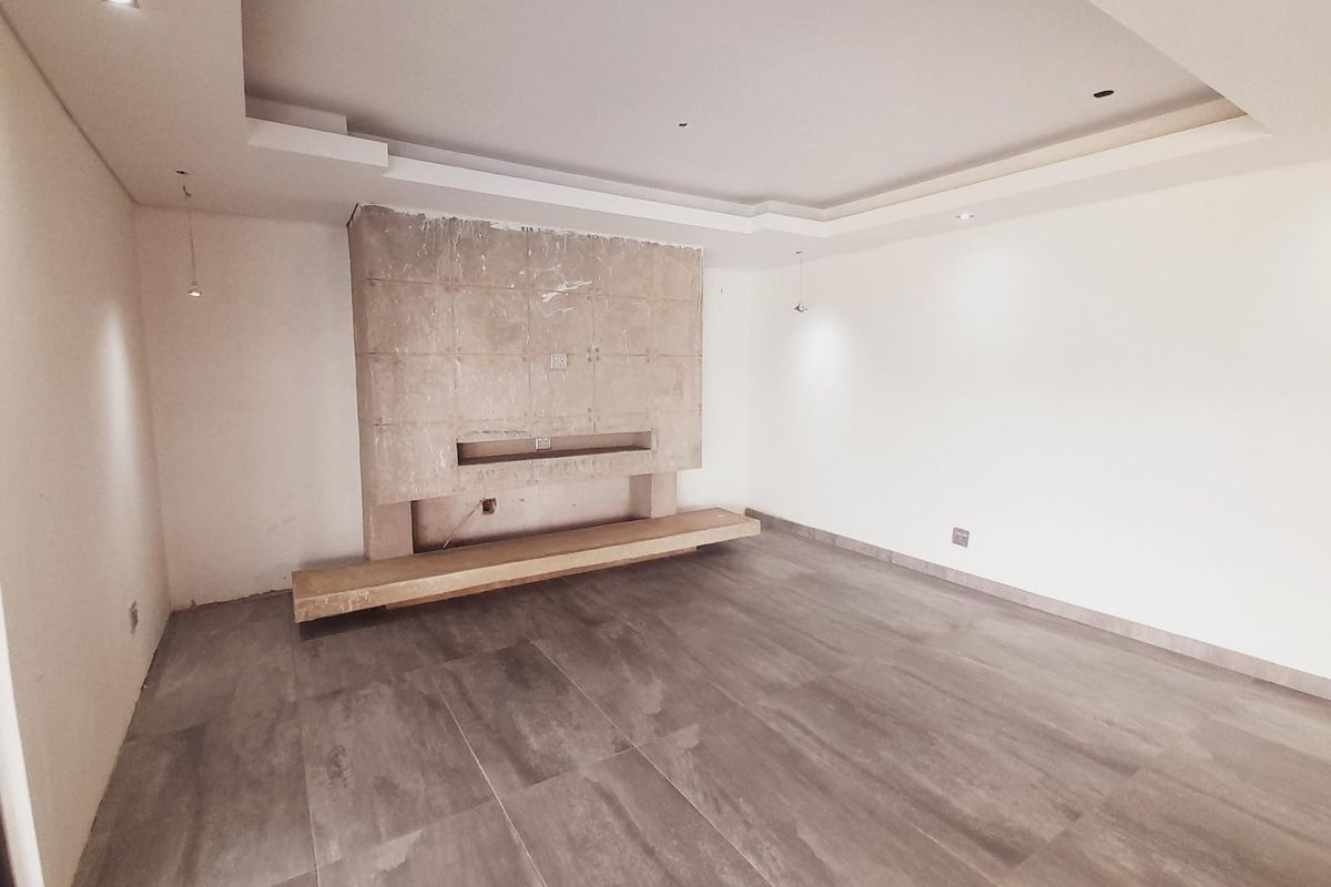 An empty living room featuring a large, unfinished stone-clad fireplace feature wall, recessed ceiling lighting, and modern grey floor tiles.