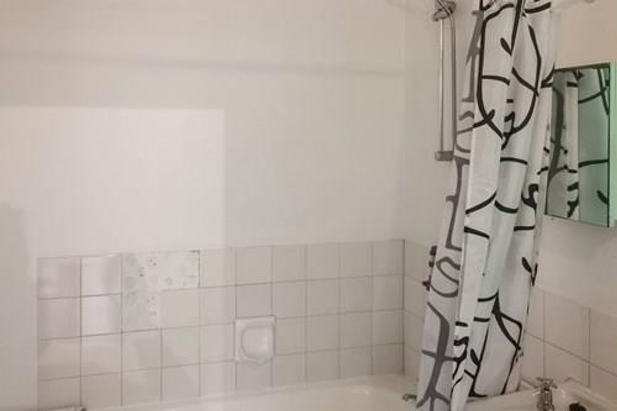 A functional bathroom featuring a bathtub with a shower head and wall tiling, currently showing signs of wear including missing tiles.