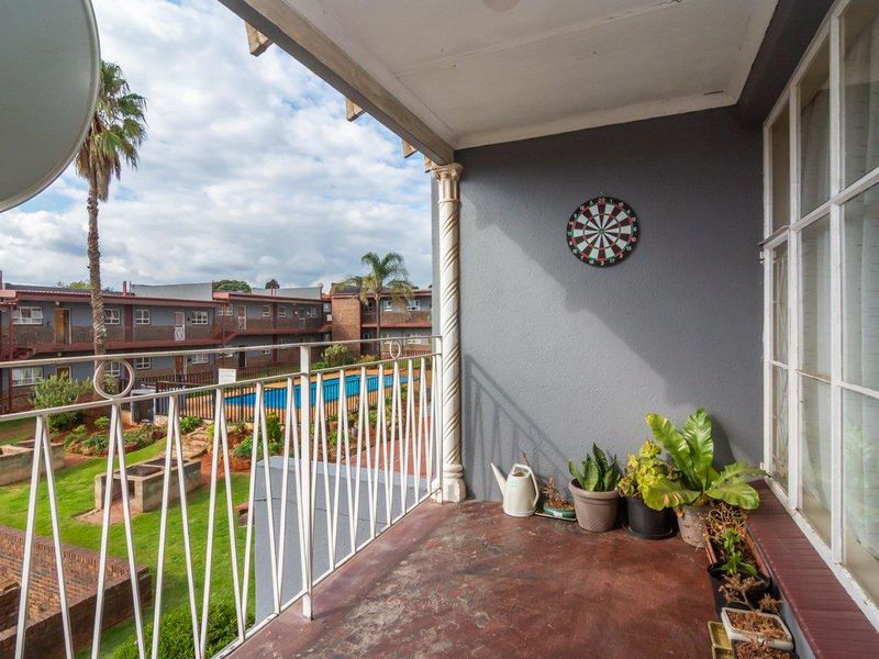 A covered balcony featuring a metal railing, overlooking the apartment complex grounds, swimming pool, and garden area.