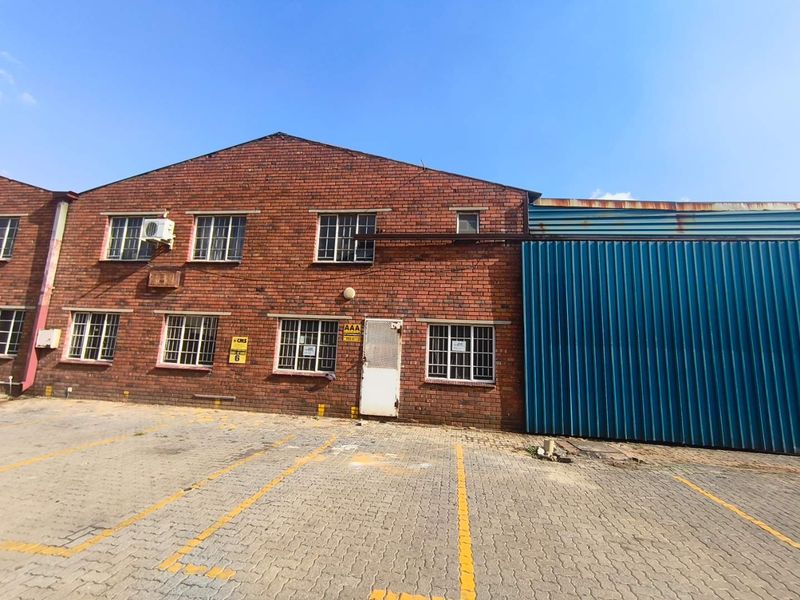 Front elevation of an industrial building featuring a brick facade, steel-framed windows with security bars, and a large blue metal roller door.