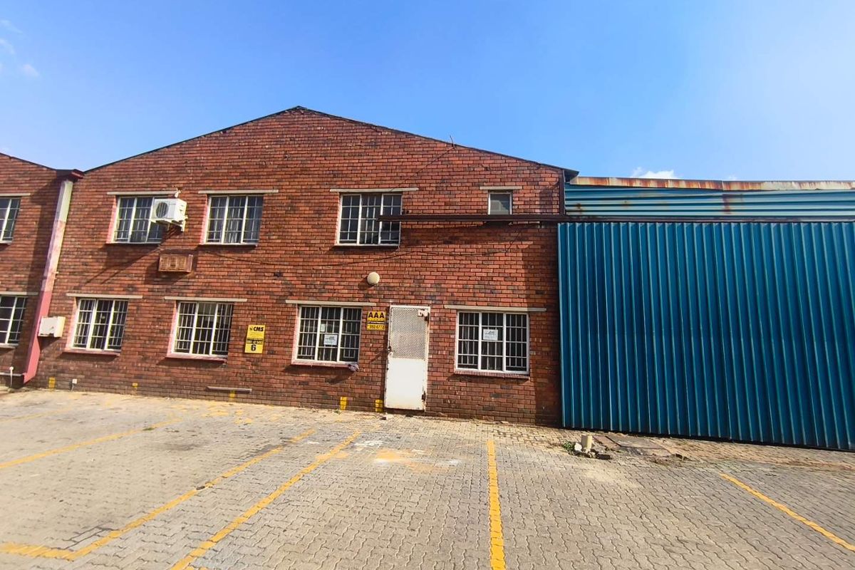 Front elevation of an industrial building featuring a brick facade, steel-framed windows with security bars, and a large blue metal roller door.