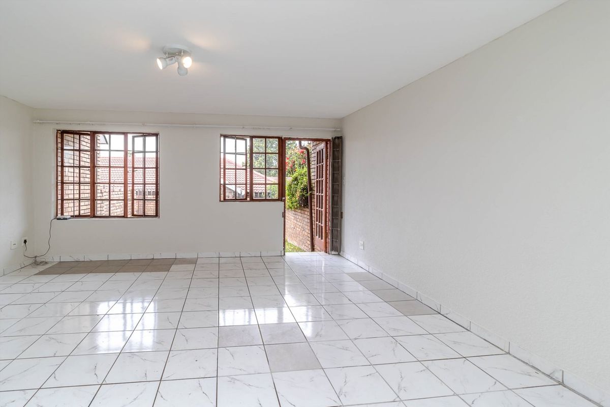 A bright, empty living area featuring white marble-look floor tiles, wooden window frames, and direct access to the rear garden through a folding door.