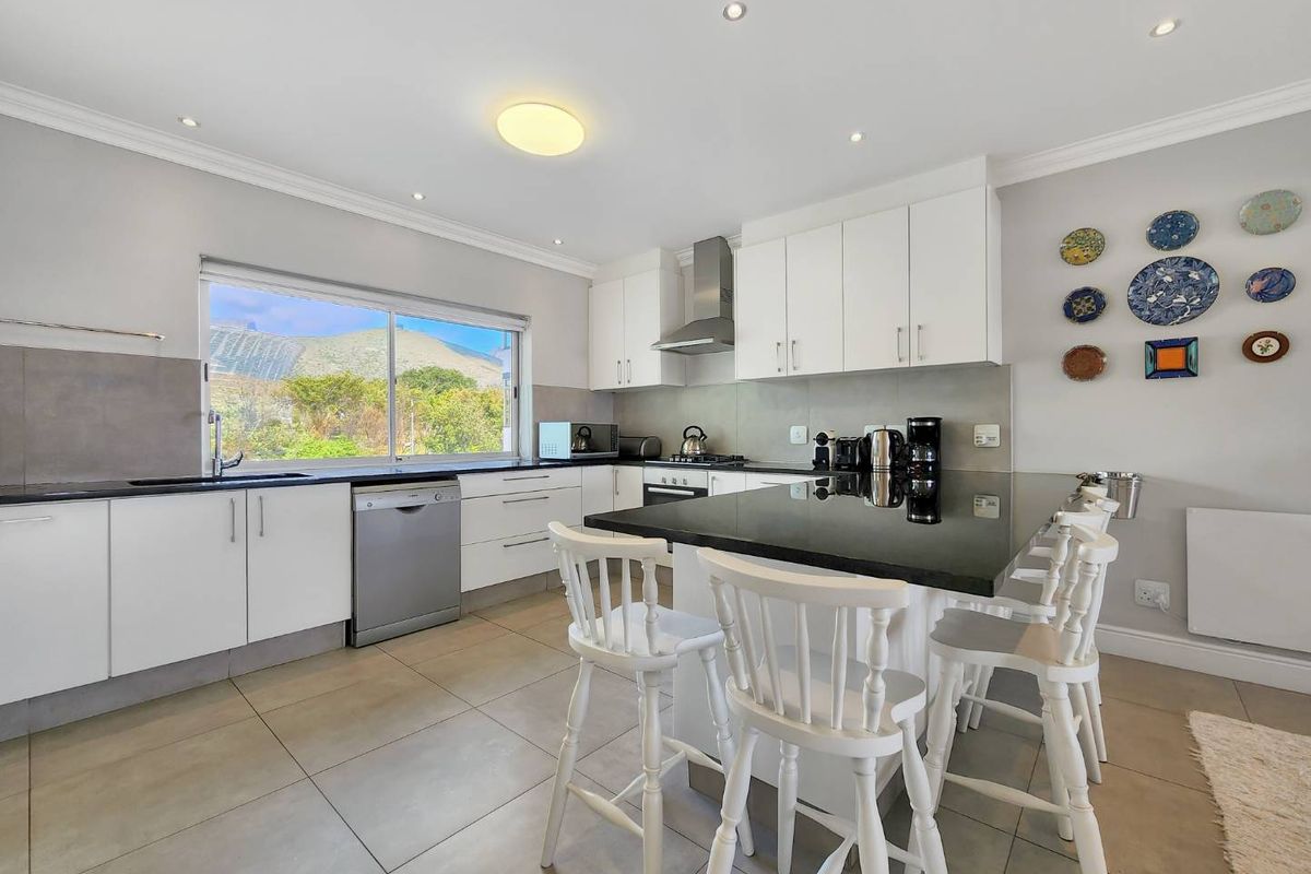 Modern kitchen featuring white cabinetry, black granite countertops, stainless steel appliances, and a central breakfast island with seating, overlooking a scenic mountain view.