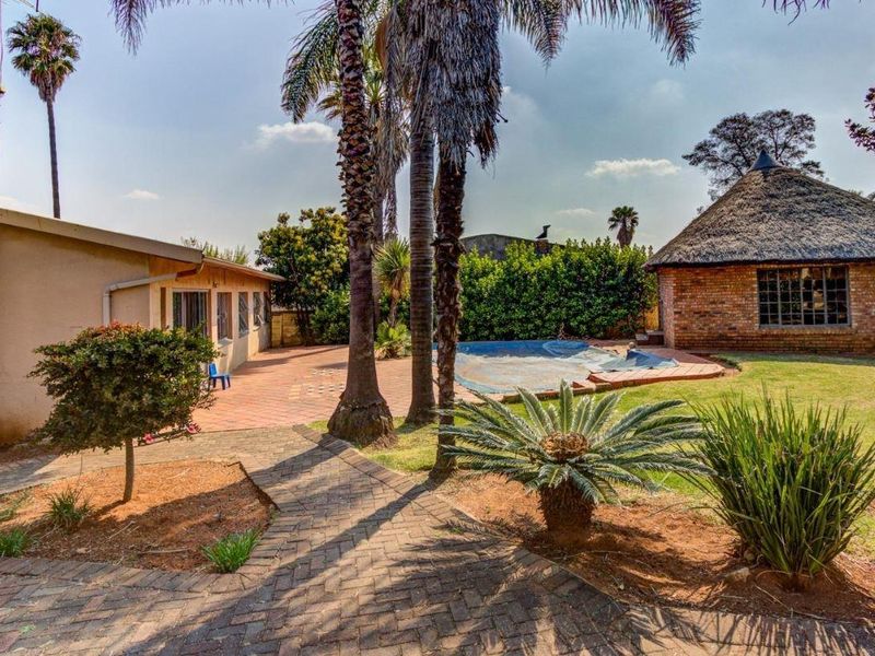 Rear garden featuring a swimming pool, paved patio area, and a traditional thatched lapa structure set within a landscaped yard.