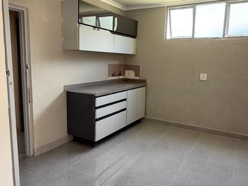 A compact, empty kitchen featuring built-in cabinetry, tiled flooring, and high-level windows, offering a blank canvas for renovation.