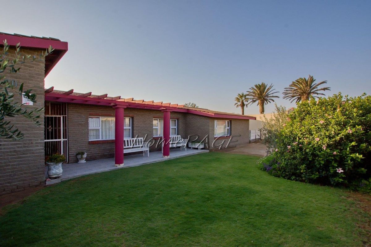 A rear exterior view of the house featuring a covered patio area with a pergola, brick facade, and a well-maintained lawn.