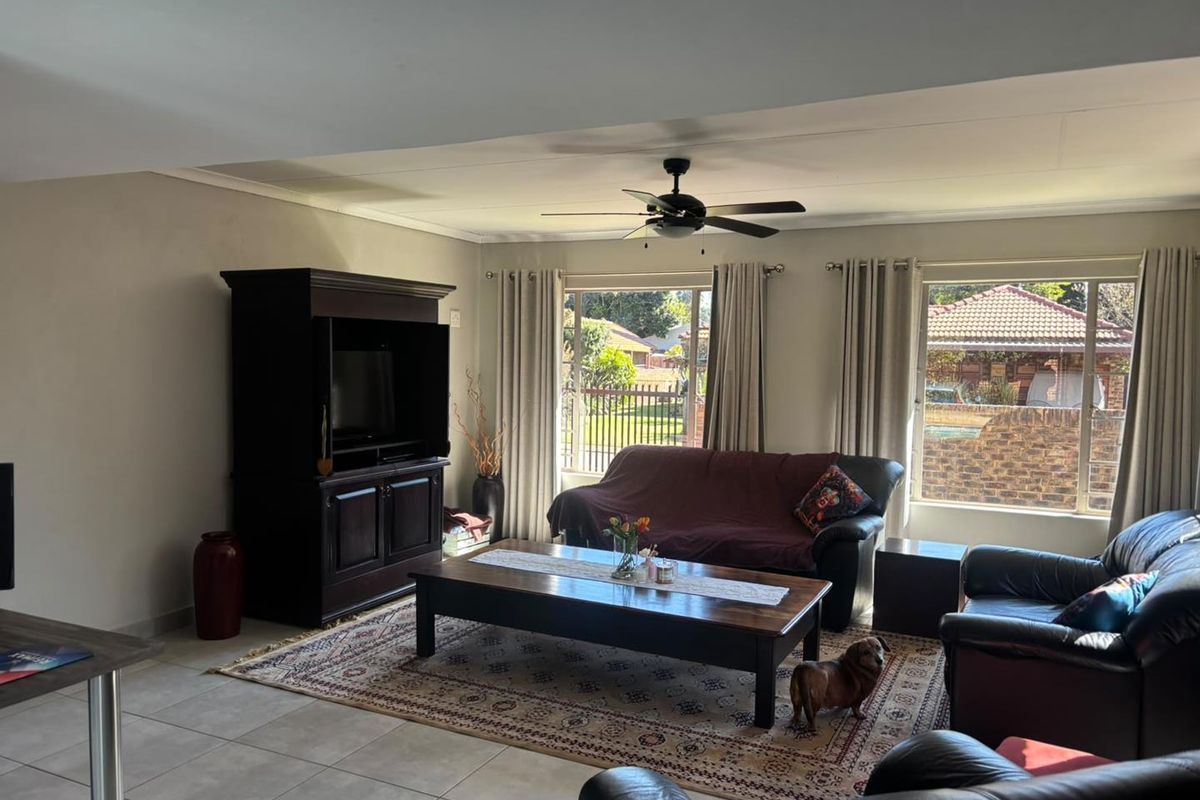 A spacious living room featuring tiled flooring, a ceiling fan, and large windows that provide natural light and views of the garden.