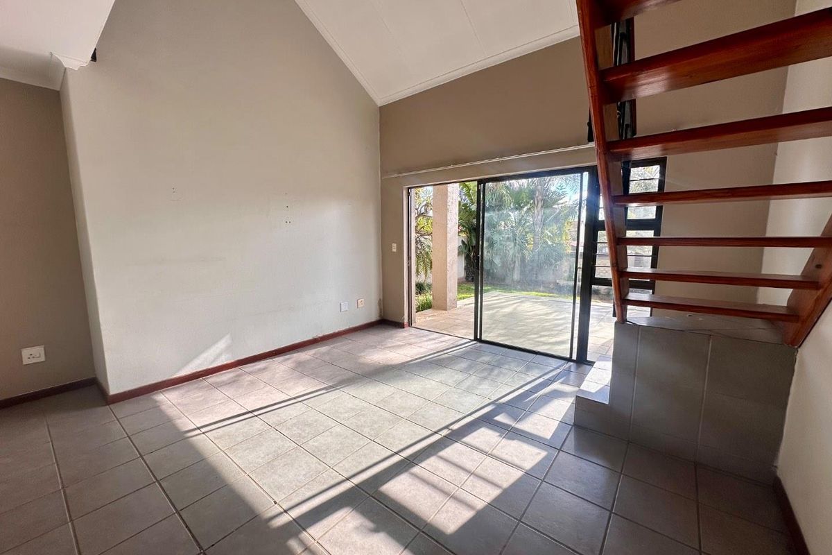 Spacious living area with high vaulted ceilings, tiled flooring, and a wooden staircase, featuring large sliding glass doors that open to a patio.