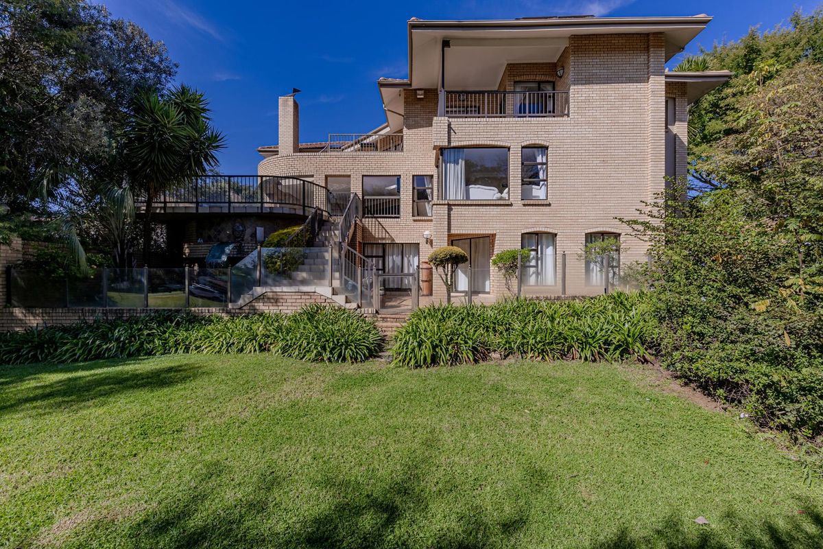 Rear view of a multi-level brick house featuring expansive balconies, glass balustrades, and a well-maintained garden area.