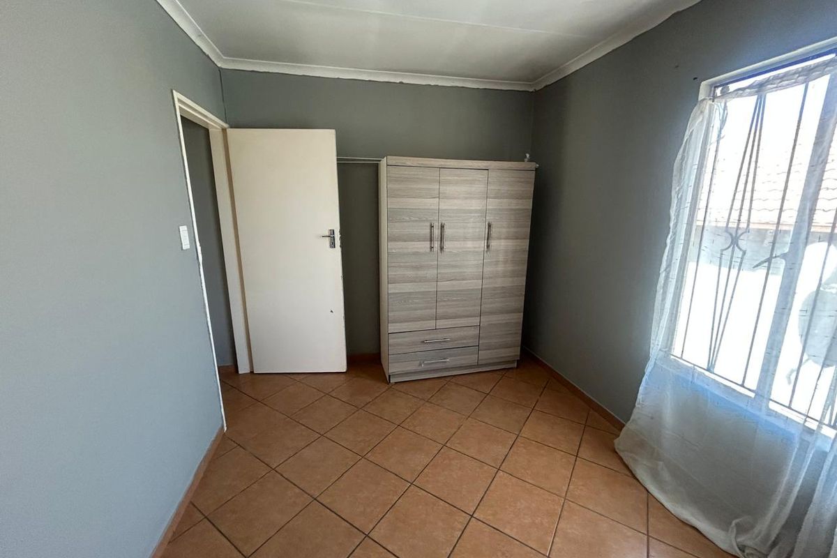 A simple bedroom featuring tiled flooring, grey painted walls, and a window with natural light.