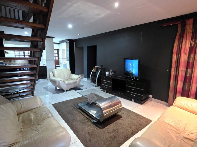 Spacious living room featuring tiled flooring, recessed downlighting, and an open-plan wooden staircase leading to the upper level.