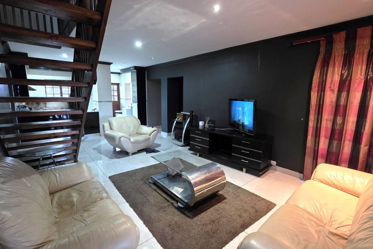 Spacious living room featuring tiled flooring, recessed downlighting, and an open-plan wooden staircase leading to the upper level.