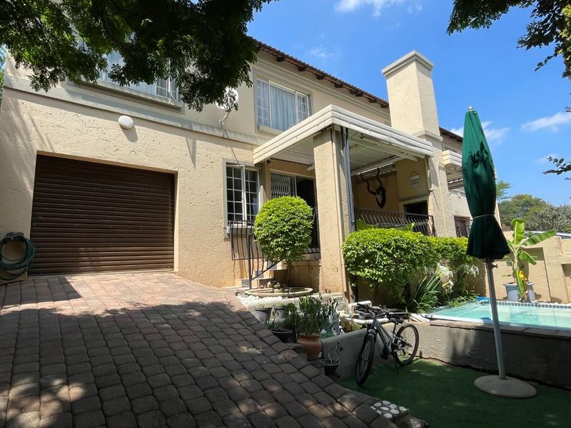 Rear exterior view of the townhouse featuring a paved driveway, attached garage, covered patio area, and a small swimming pool.