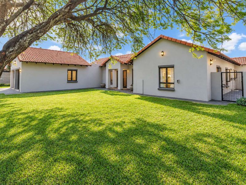 A well-maintained rear exterior view of the house featuring a spacious lawn, terracotta tiled roof, and paved access paths.