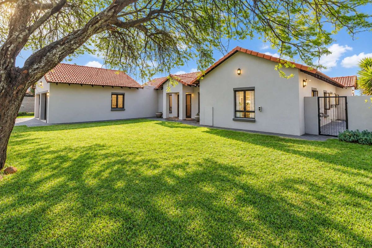 A well-maintained rear exterior view of the house featuring a spacious lawn, terracotta tiled roof, and paved access paths.