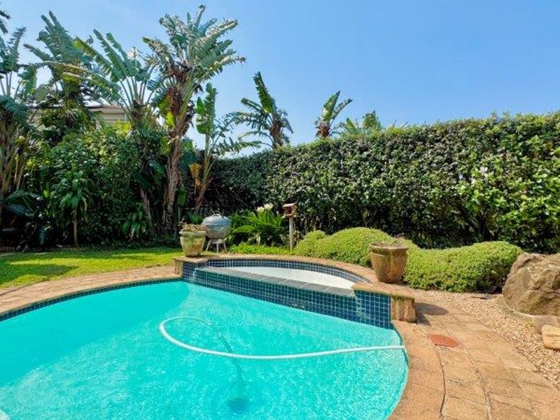 A well-maintained private swimming pool area featuring a tiled surround, established garden landscaping, and mature privacy hedging.