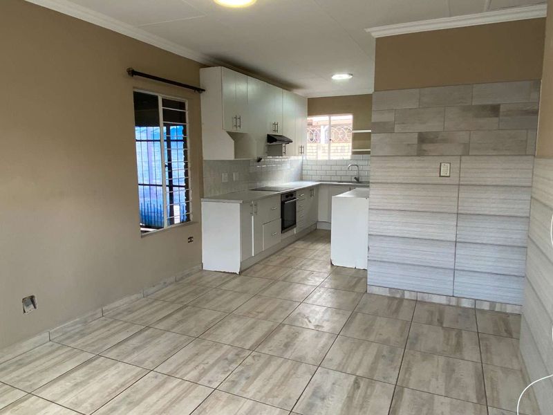 Open-plan kitchen and living area featuring tiled flooring, white cabinetry, built-in oven and hob, and neutral wall tones.
